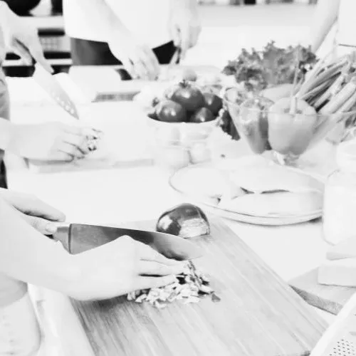 Mains qui émincent des légumes sur une planche, pendant un cours de cuisine